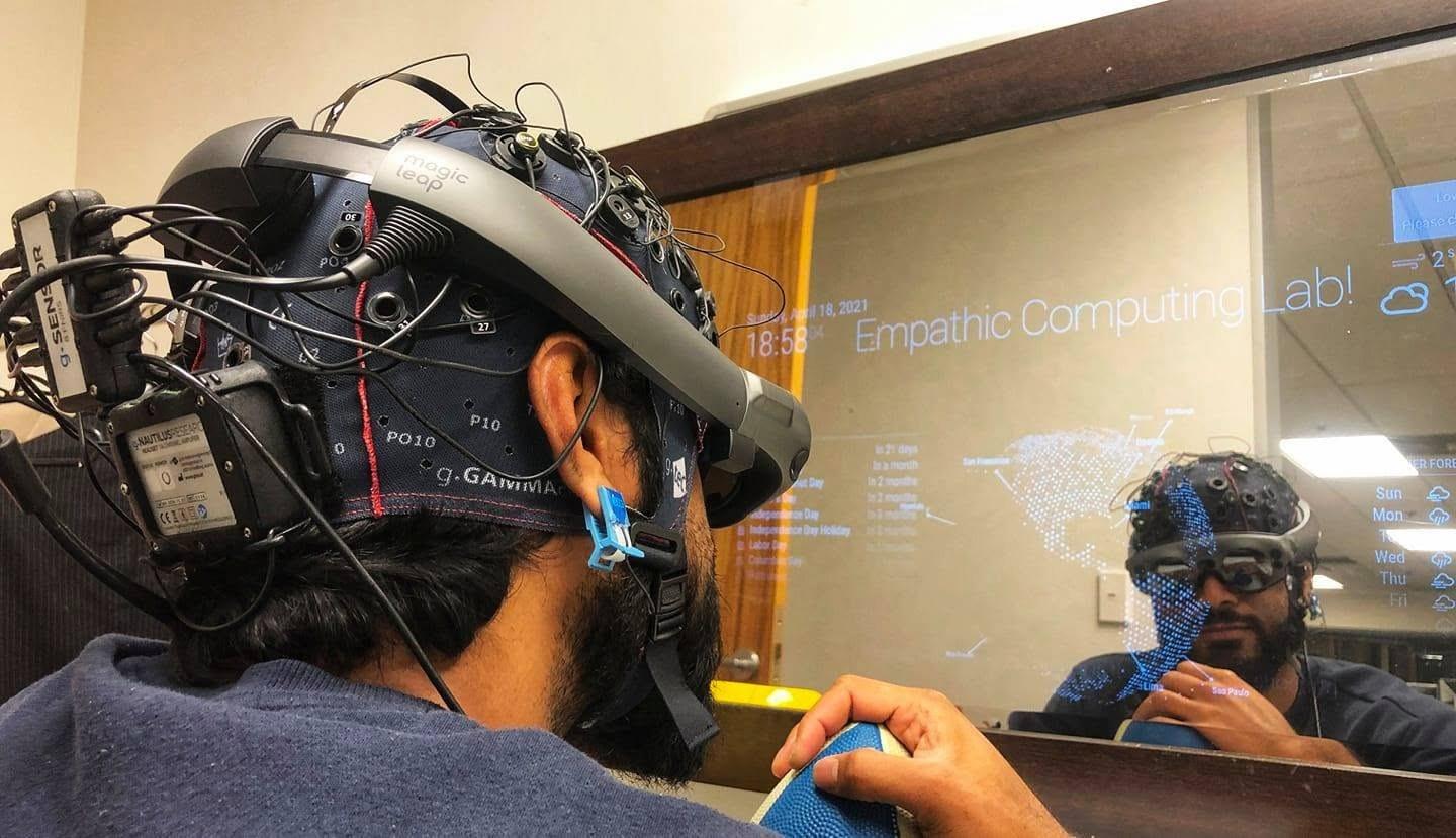 Every wire here is a thing that can go wrong Me at the Empathic Computing Lab wearing a g.tec fNIRS cap and a Magic Leap 2 at the same time, in front of a mirror display reading my state back to me.